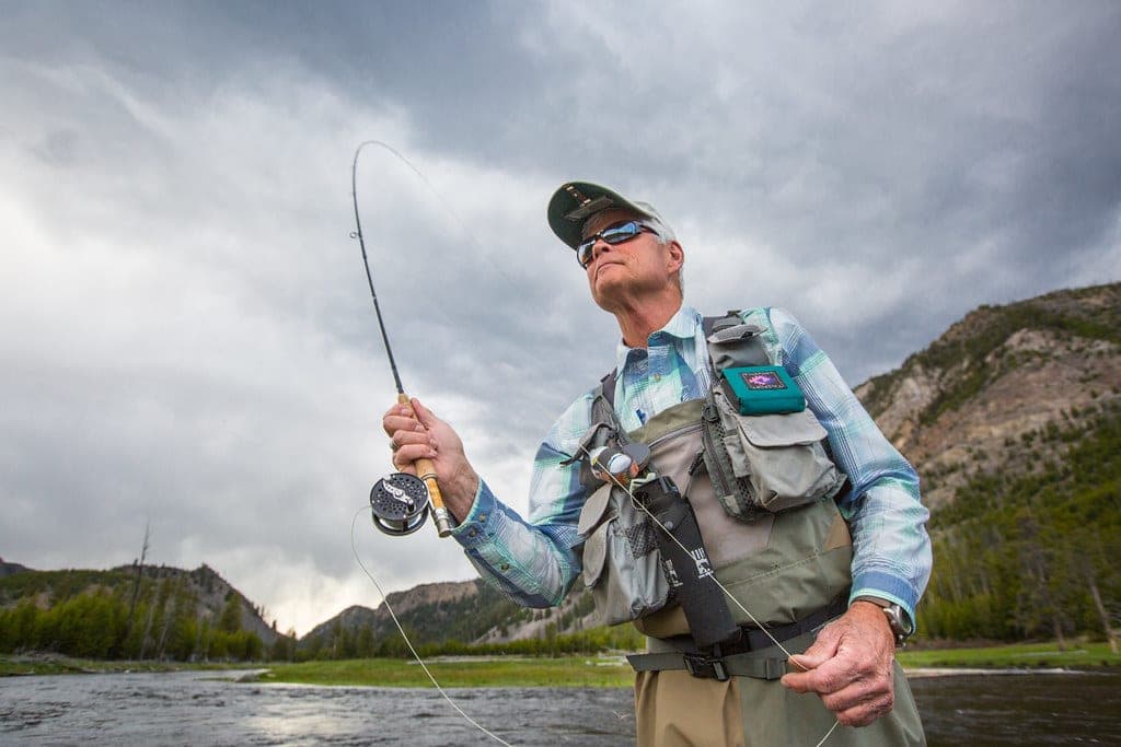 A fly angler casting a line across a shallow river in early morning light