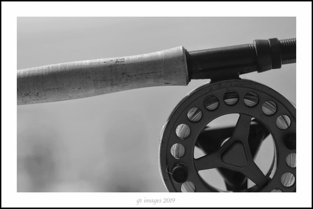 A fly rod and reel resting on river gravel beside flowing water